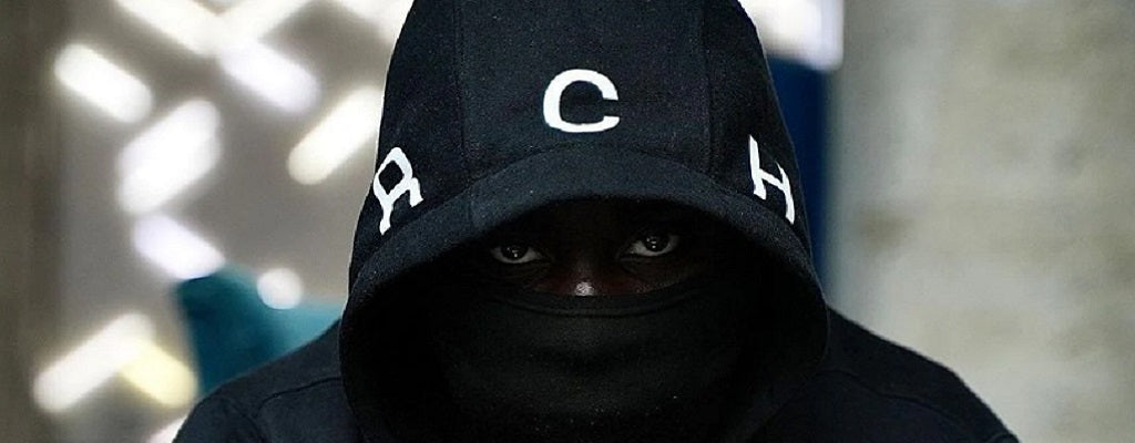 Personne portant une cagoule noire sous une capuche ornée de lettres blanches, avec un regard intense – illustration du mystère et de l'impact visuel des balaclavas dans la mode et la culture urbaine.