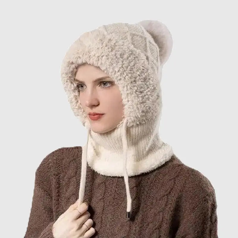 Femme portant un bonnet cagoule tricot BEIGE avec doublure en fausse fourrure douce, pompon décoratif et cordons ajustables, idéal pour se protéger du froid en hiver.