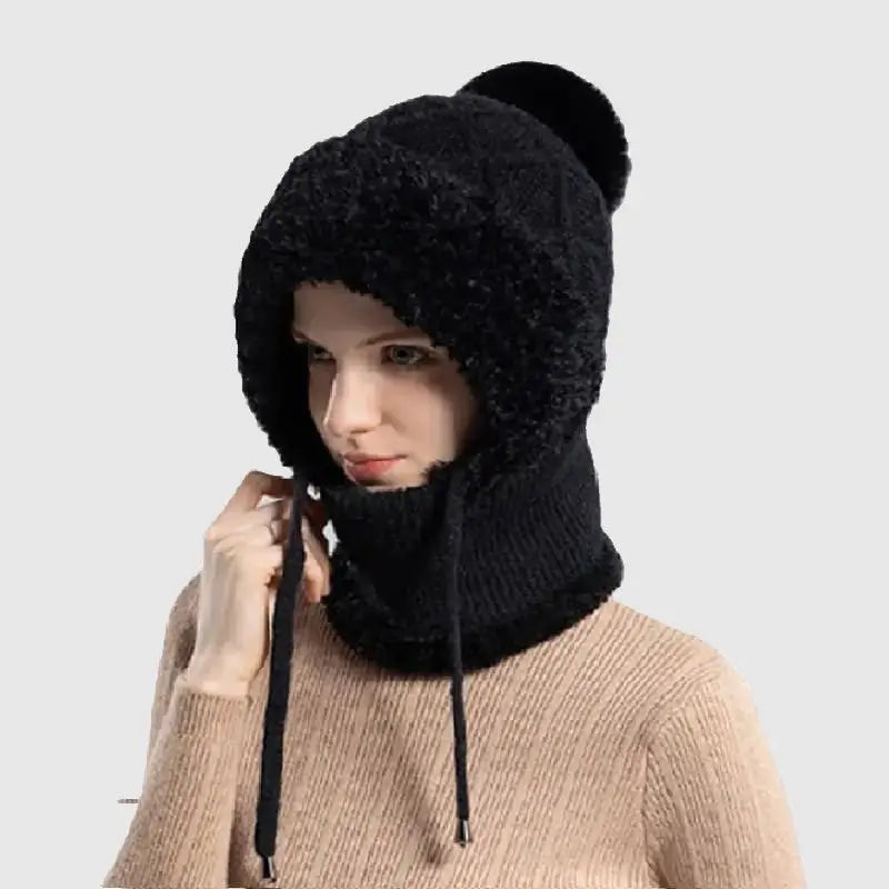 Femme portant un bonnet cagoule tricot noir avec une doublure chaude en fausse fourrure, pompon élégant et cordons ajustables, idéal pour l'hiver et les activités extérieures.