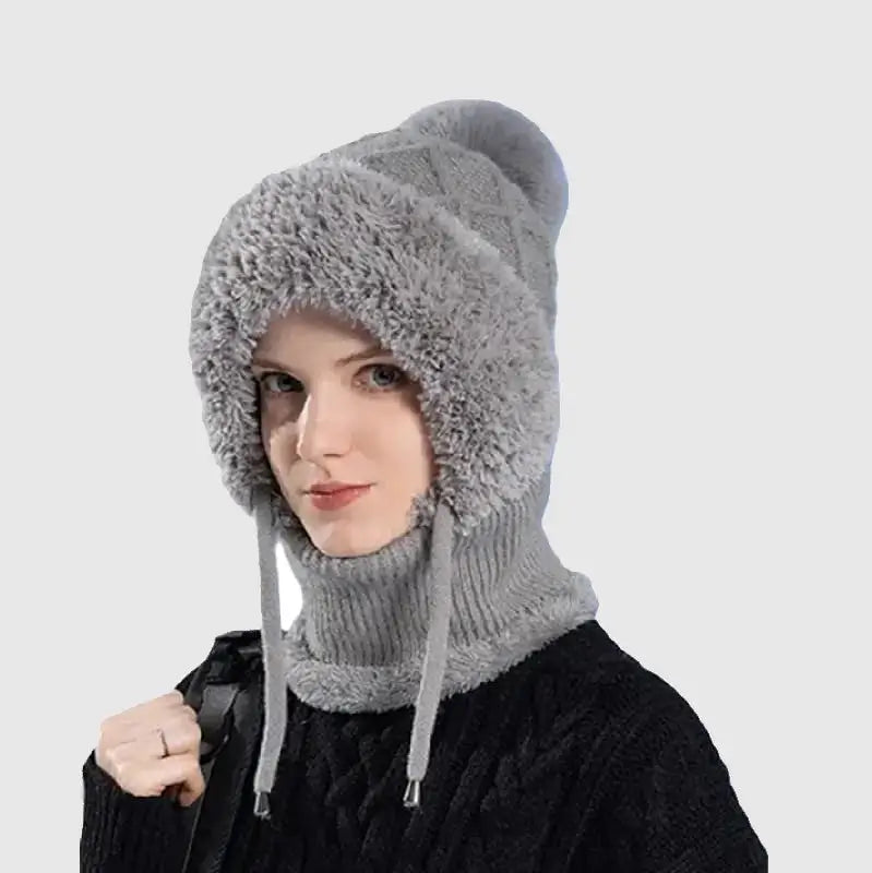 Femme vêtue d'un bonnet cagoule tricot gris, doté d'une doublure en fausse fourrure douce et cordons ajustables, parfait pour protéger du froid en hiver ou lors d'activités outdoor.