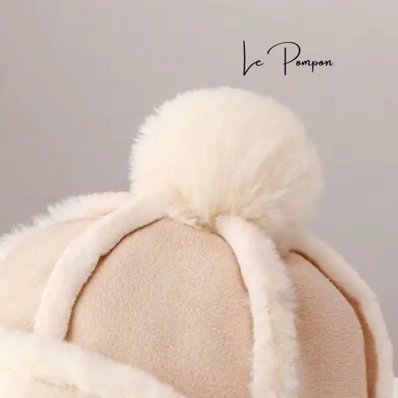 Gros plan sur le pompon d’un Bonnet Chapka Enfant beige et blanc, mettant en avant la texture douce et duveteuse de l’accessoire d’hiver.