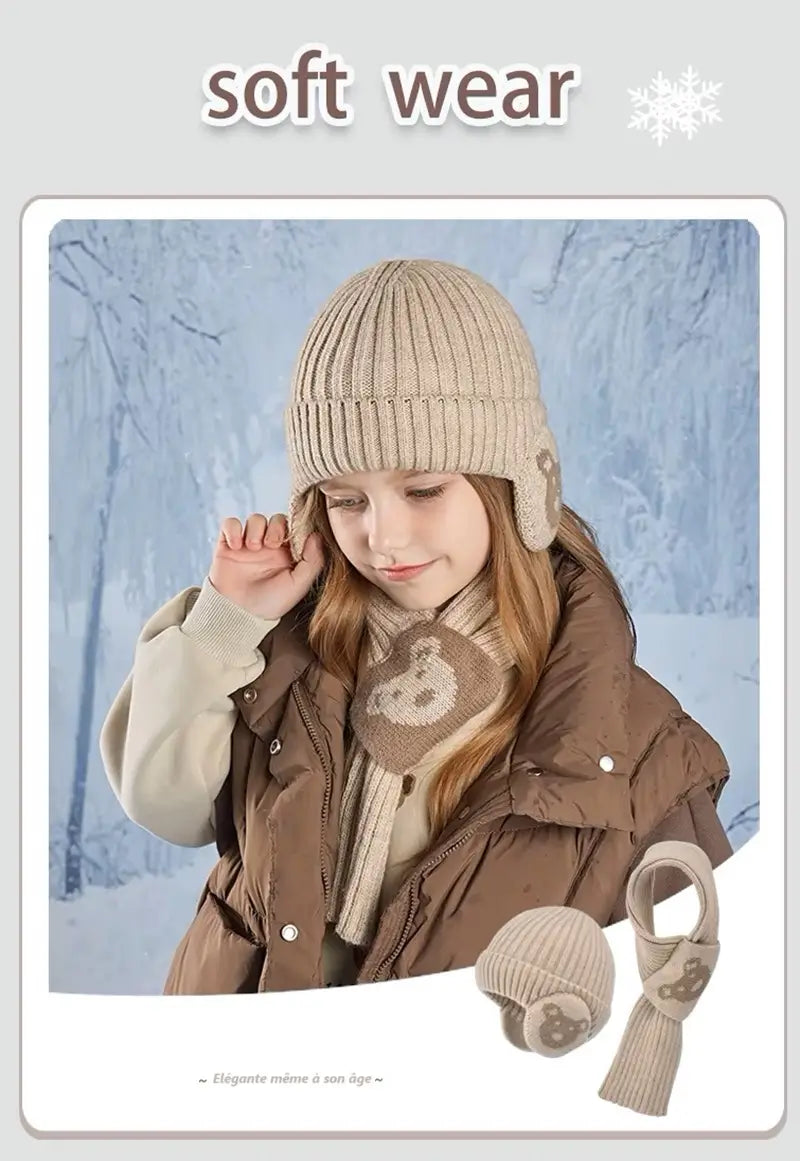 Fille portant un ensemble bonnet écharpe enfant en tricot beige avec des motifs d'ours, associée à une veste matelassée marron, posant sur un fond hivernal givré. La présentation inclut un aperçu du bonnet et de l'écharpe assortis, sous le titre 'soft wear' avec des flocons de neige décoratifs.