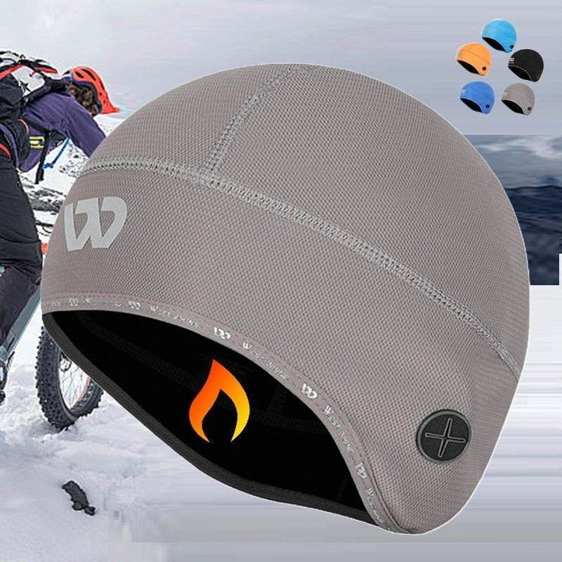 Bonnet sous casque vélo gris avec doublure polaire, porté par un cycliste en montagne sous la neige. Accessoire idéal pour le vélo par temps froid.