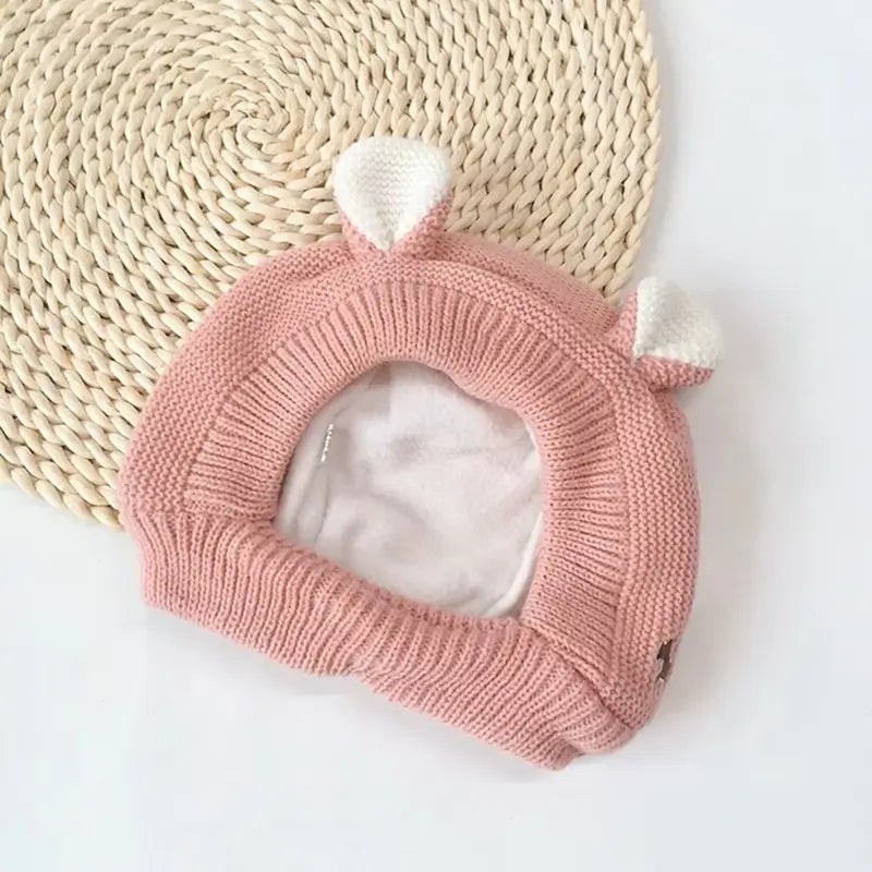 Cagoule bébé 6 à 24 mois rose en tricot doux, avec des petites oreilles blanches et doublure chaude en polaire. Idéale pour protéger la tête et le cou du froid.