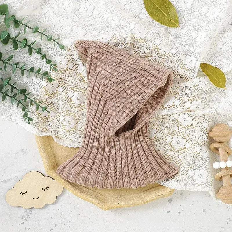 Cagoule bébé kaki en tricot, mise en valeur sur un fond naturel, offrant une option chaude et élégante pour les sorties hivernales.