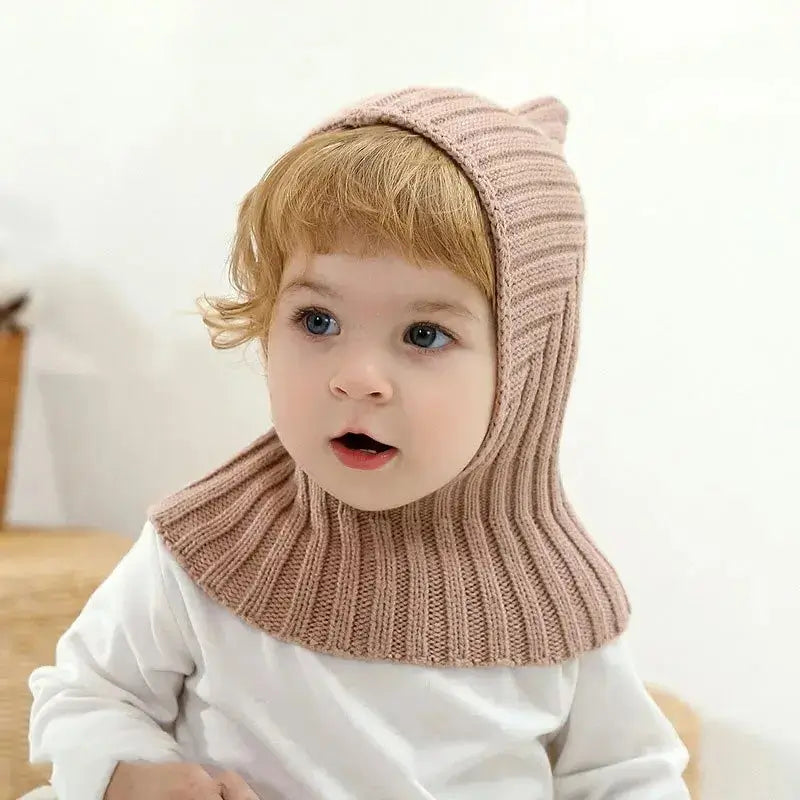 Bébé portant une cagoule kaki en tricot avec un design couvrant et ajusté, offrant chaleur et protection pendant les journées froides. Cagoule bébé pratique et élégante.