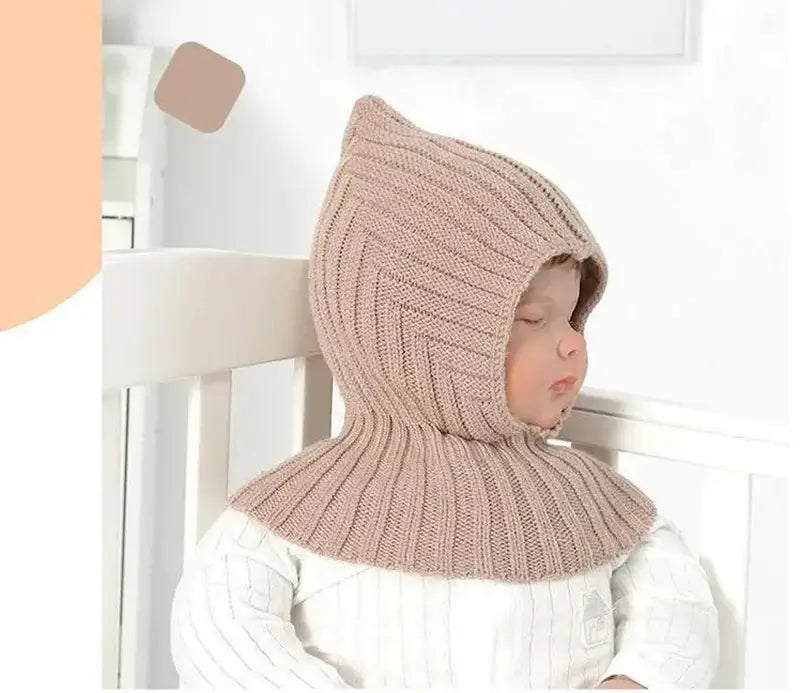 Bébé paisible portant une cagoule kaki en tricot, offrant une protection contre le froid tout en étant confortable pour dormir. Cagoule bébé adaptée aux températures hivernales.