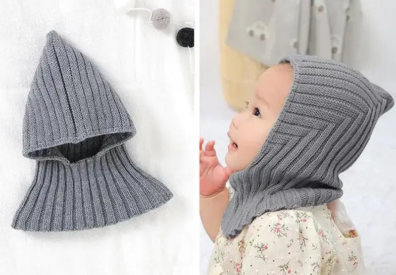 Bébé portant une cagoule grise en tricot, couvrant la tête et le cou, parfait pour les journées froides, tout en restant confortable et tendance. Cagoule bébé adaptée pour l'hiver.