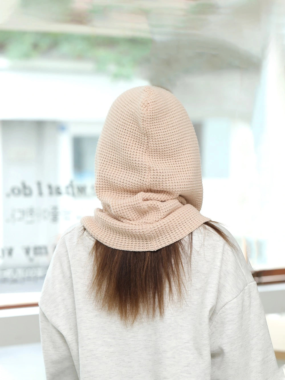 Vue arrière d'une femme portant une cagoule cache cou femme beige en laine, couvrant les cheveux et le cou, dans un environnement intérieur lumineux.