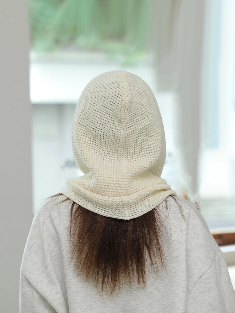 Vue arrière d’une femme avec une cagoule cache cou femme blanche couvrant la tête et le cou, laissant apparaître ses longs cheveux bruns.