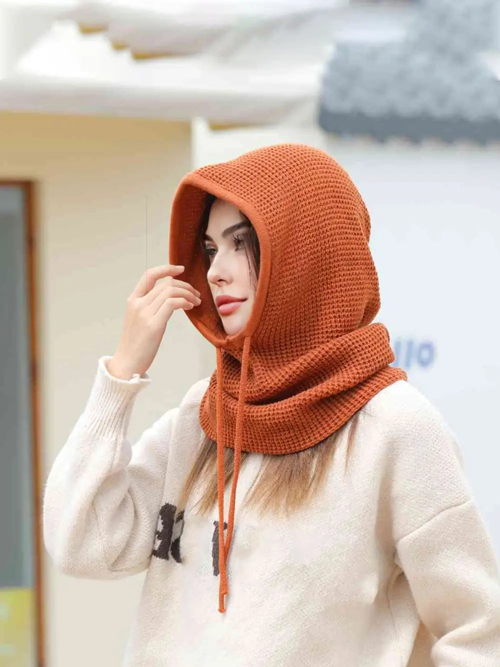 Femme portant une cagoule cache cou femme couleur rouille, capuche relevée, ajustant les cordons pour un ajustement parfait en extérieur.