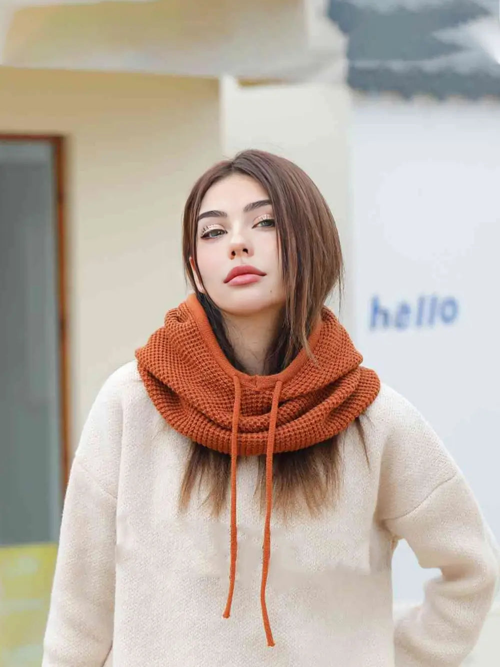 Femme debout avec une cagoule cache cou femme couleur rouille, capuche abaissée, posant en extérieur avec un look élégant et chaleureux