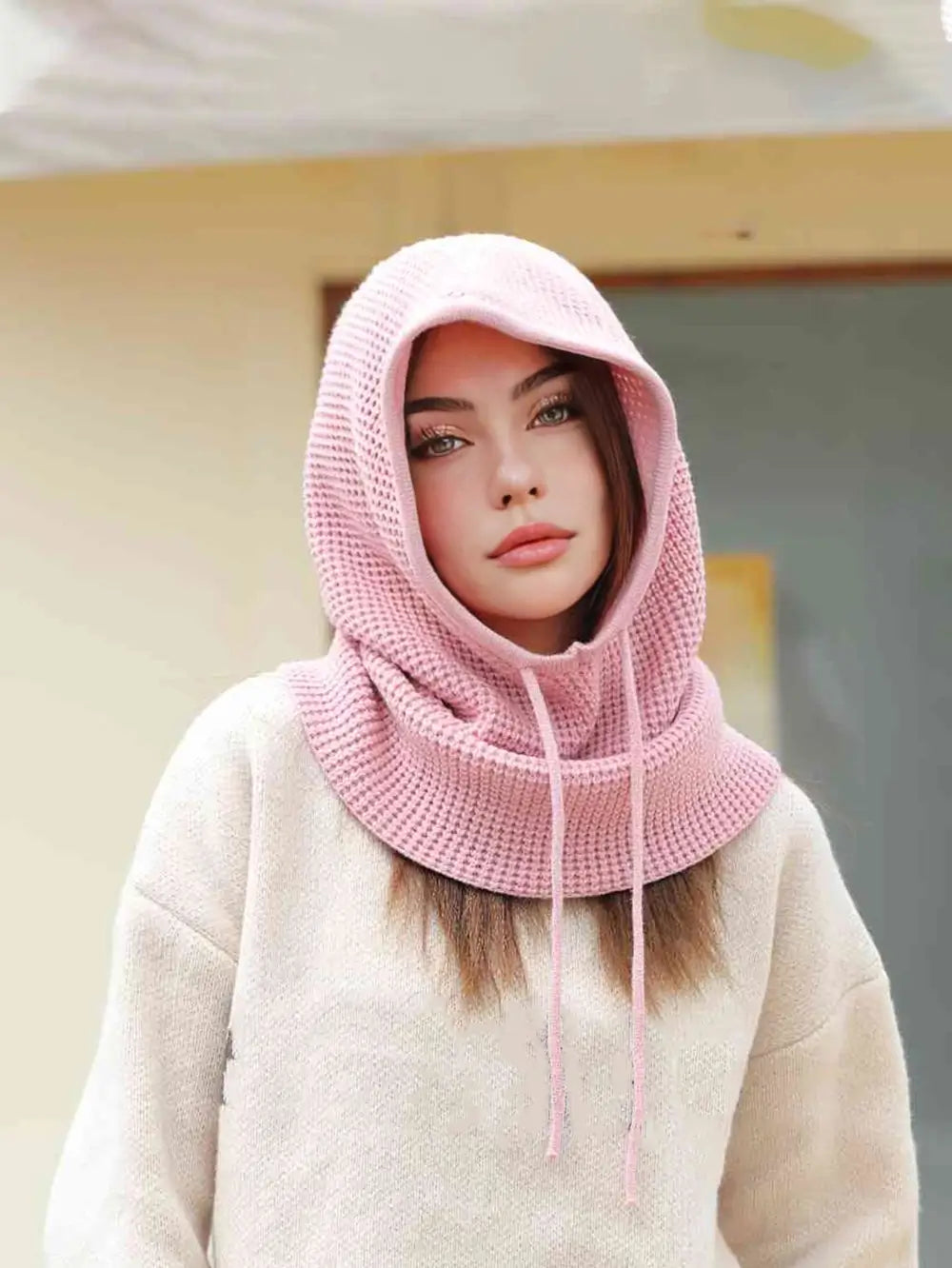 Femme portant une cagoule cache cou femme rose, capuche relevée avec cordons, offrant une protection élégante contre le froid en extérieur