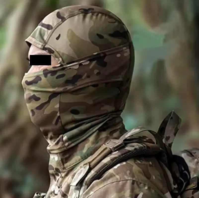 Cagoule camouflage militaire en motif forêt portée par un soldat, équipée d’un sac à dos tactique, dans un environnement boisé.