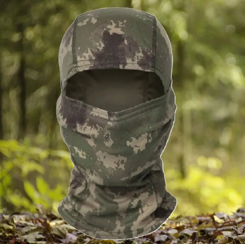 Cagoule-camouflage-militaire dans des tons verts et marrons, offrant une couverture complète du visage et du cou, idéale pour les activités de plein air comme la chasse ou l'airsoft, présentée dans un environnement forestier.