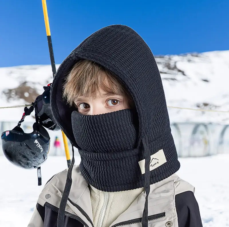 Cagoule Enfant Hiver noire avec tour de cou, portée par un garçon dans un environnement enneigé. Parfaite pour maintenir chaleur et confort pendant les sports d’hiver.