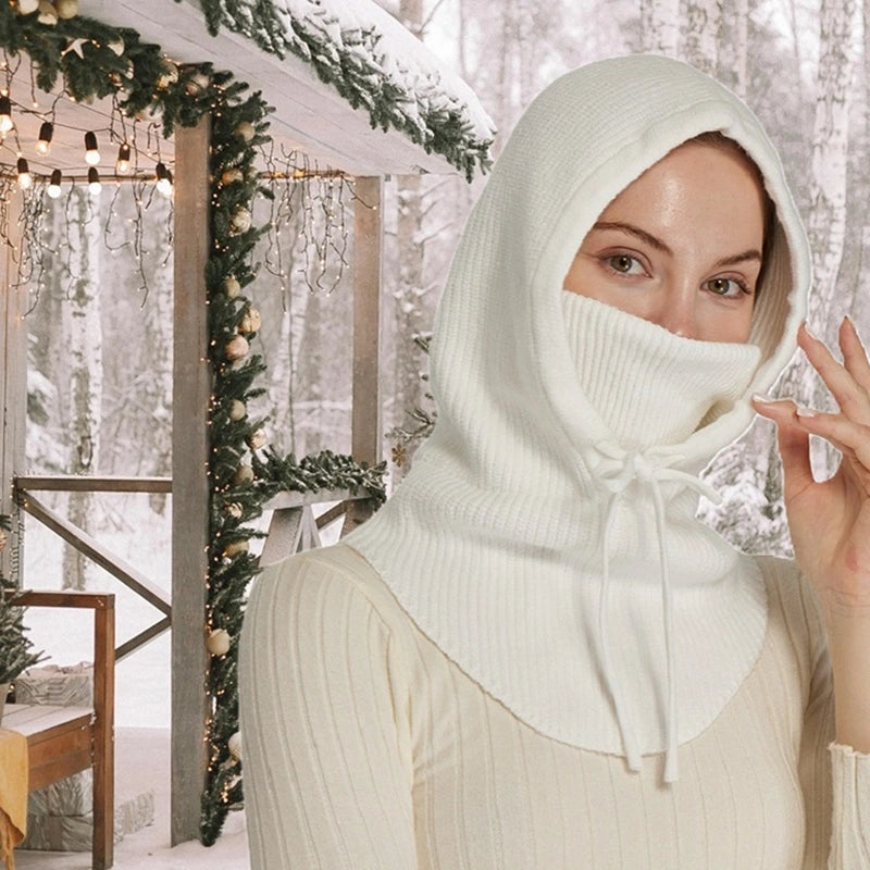 Femme habillée d'une cagoule blanche avec tour de cou intégré, ajustable grâce à des cordons, dans un cadre extérieur festif sous la neige. Accessoire idéal pour rester au chaud.