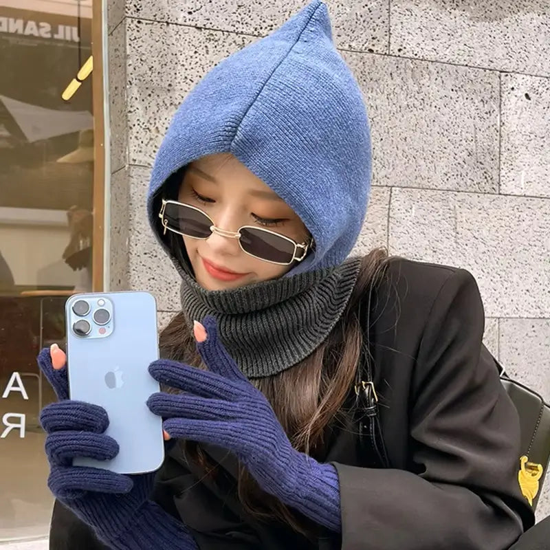 Jeune femme portant une cagoule femme en laine bleue avec col gris, des lunettes de soleil élégantes et des gants assortis en laine bleu marine, tenant un iPhone dans un environnement urbain moderne.