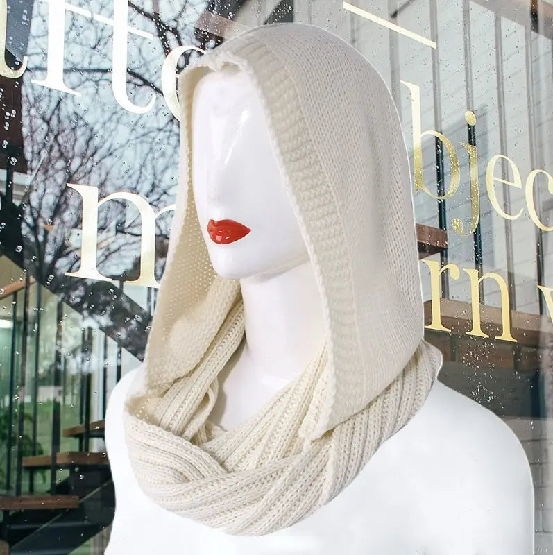 Mannequin présentant une cagoule femme en tricot beige avec capuche ample et écharpe intégrée, un accessoire tendance pour un look mode et chaleureux en hiver.