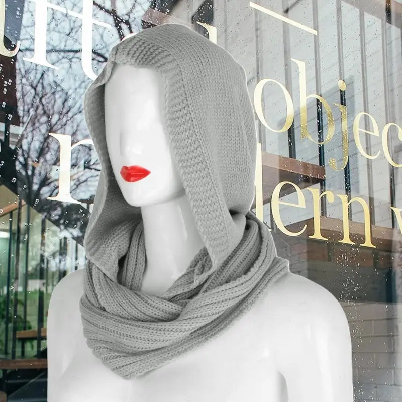 Mannequin portant une cagoule femme en tricot gris clair avec capuche ample et écharpe intégrée, idéale pour un look mode élégant et chaleureux en hiver.