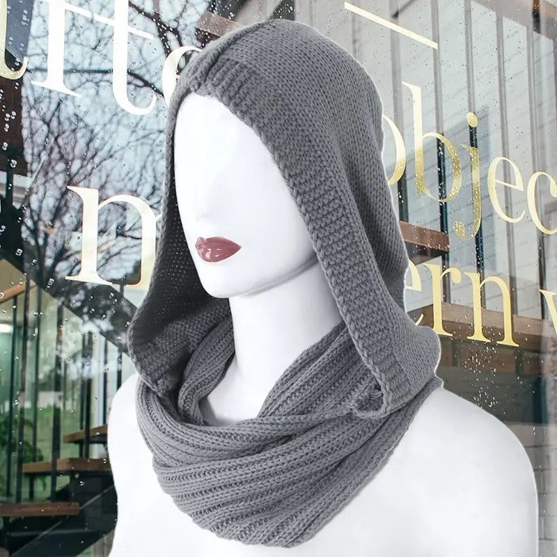 Mannequin portant une cagoule femme en tricot gris foncé avec une capuche ample et une écharpe intégrée, élégante et pratique pour un look mode hivernal moderne