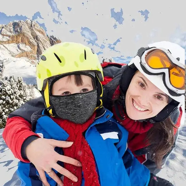 Deux enfants en plein air, souriant avec des casques colorés et des cagoules fines sous casque enfant grises, au milieu d'un paysage de montagne enneigée.