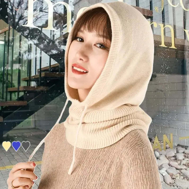 Femme portant une cagoule hiver femme beige en maille avec cordons ajustables, couvrant la tête et le cou. Fond urbain avec un léger flou.