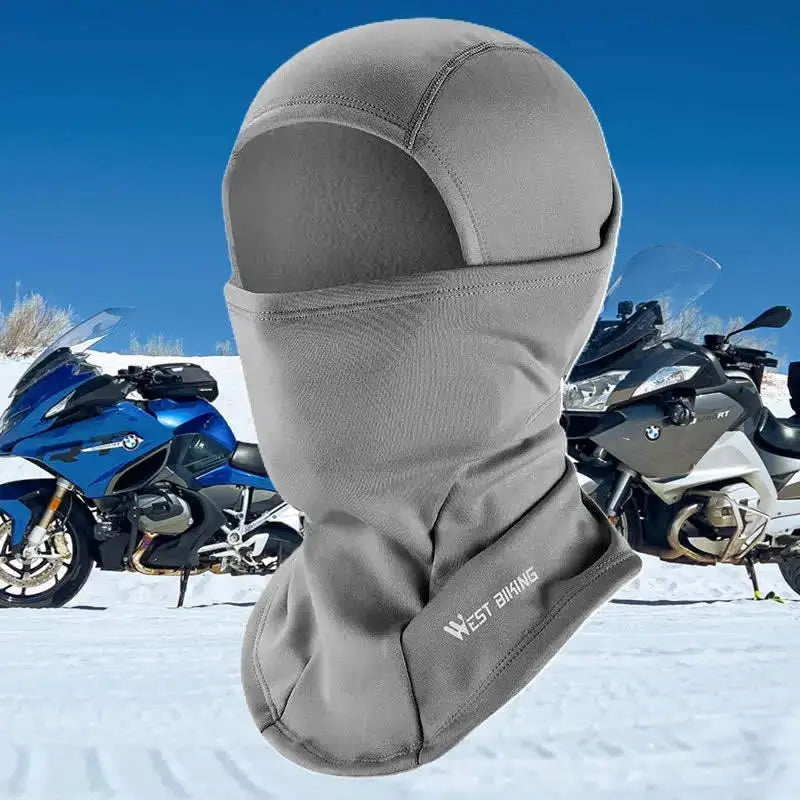 Cagoule hiver pour moto grise, offrant une protection thermique et un confort optimal, idéale pour les balades hivernales en montagne. Présentée sur fond enneigée avec Motos en arrière plan.