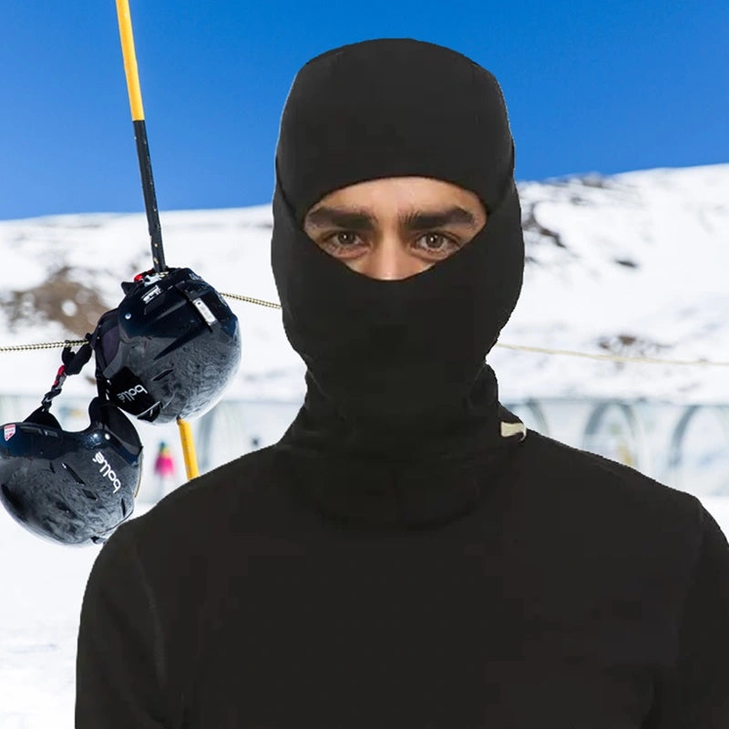 Homme, vue de face dans un environnement enneigé et portant une cagoule en laine mérinos noire, , couvrant la tête et le cou, offrant une protection intégrale contre le froid tout en restant respirante et confortable.