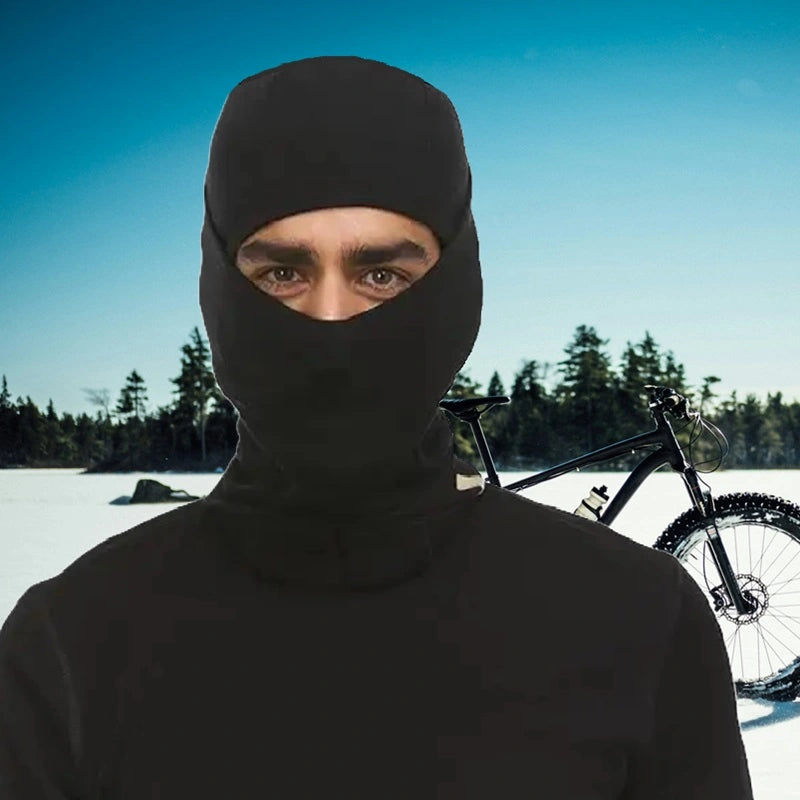 Cycliste portant une cagoule en laine mérinos noire dans un paysage hivernal avec des arbres enneigés, parfaite pour les cyclistes recherchant confort et protection.