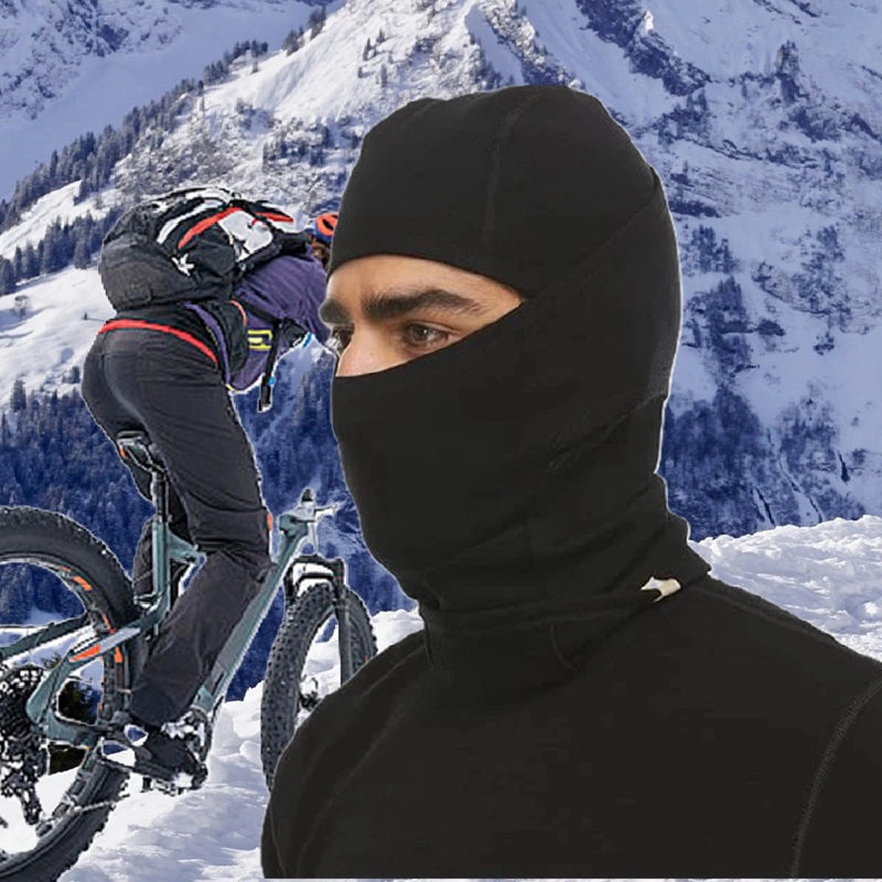 Cycliste portant une cagoule en laine mérinos noire dans un environnement montagneux enneigé, idéal pour les sorties à vélo en hiver et par temps froid.