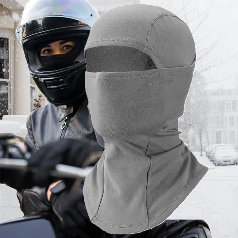 Cagoule moto femme grise, conçue pour protéger le visage et le cou du froid, idéale pour les trajets hivernaux à moto. En arrière-plan, une motarde équipée et prête à rouler sous la neige.