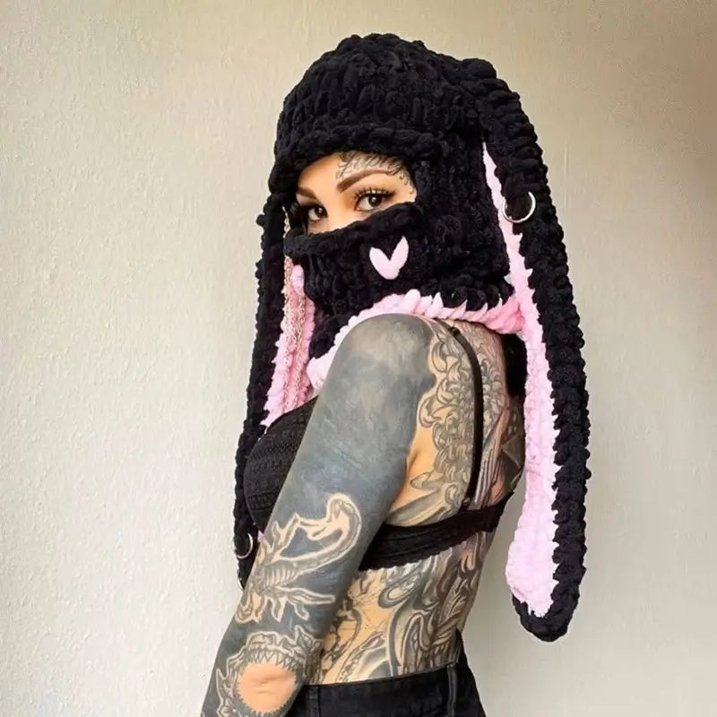 Cagoule Oreilles de lapin noire et rose sur mannequin tatoué – Une femme tatouée porte une cagoule noire avec de longues oreilles de lapin doublées de rose clair. Un look audacieux et cosy, parfait pour un style streetwear hivernal.