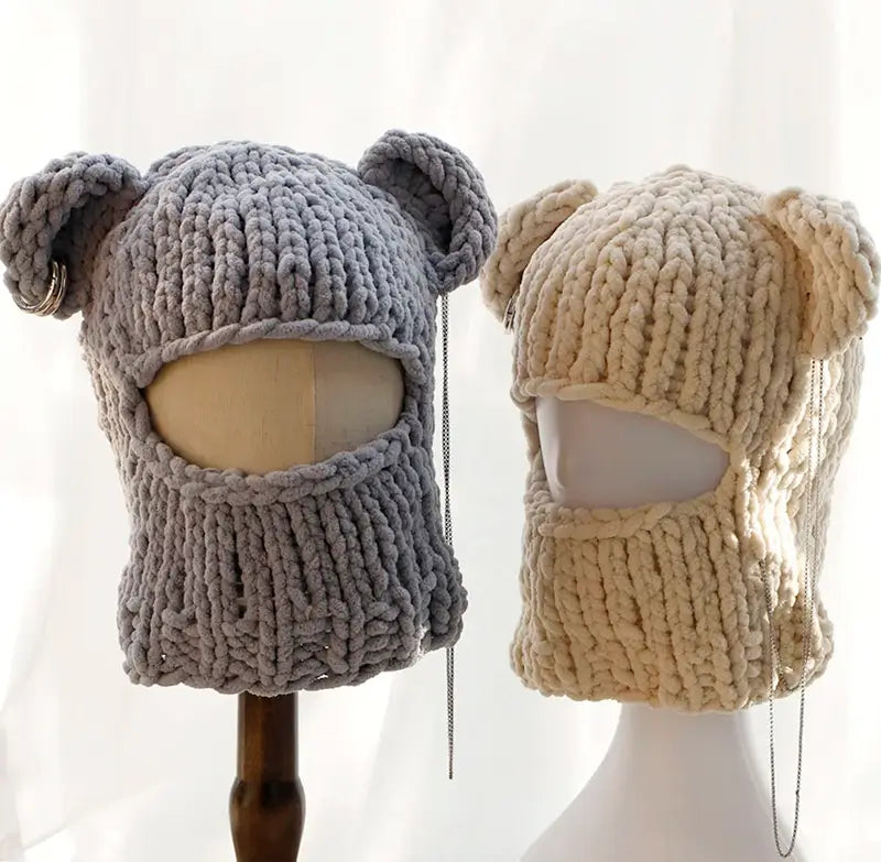 Deux cagoules oreilles en tricot, une grise et une beige, exposées sur des mannequins avec un design couvrant le visage, parfaites pour l'hiver.