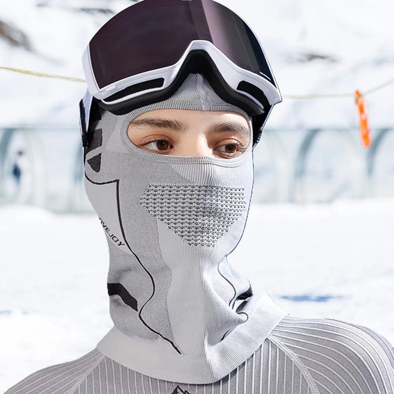 Femme portant une cagoule ski femme gris clair sous un masque de ski dans un paysage enneigé. Tissu respirant et protection intégrale du visage et du cou.