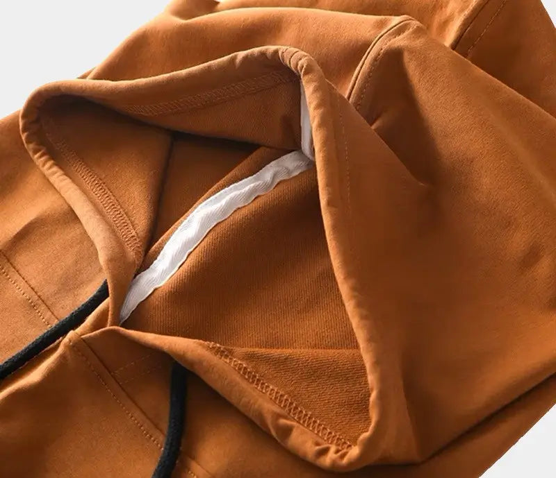 Gros plan sur une cagoule streetwear marron en coton avec coutures renforcées. Les détails de finition et les cordons noirs soulignent la qualité et le confort de cet accessoire tendance, parfait pour un look urbain.