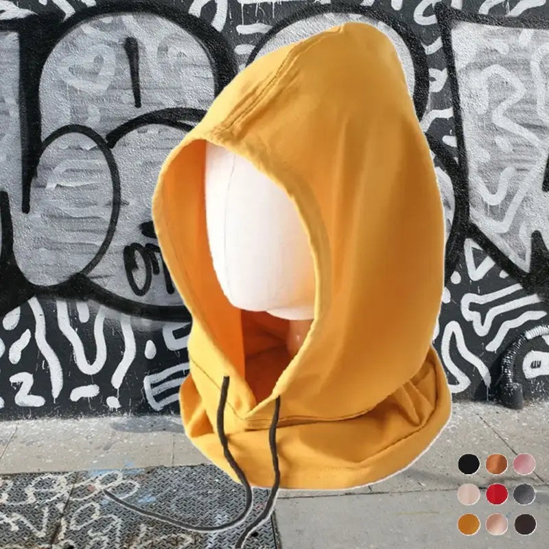 Cagoule streetwear jaune moutarde avec capuche large et cordons ajustables. L'arrière-plan urbain avec des graffitis noirs et blancs renforce l'esthétique streetwear. Confortable et tendance, cette cagoule est idéale pour un style moderne et décontracté.