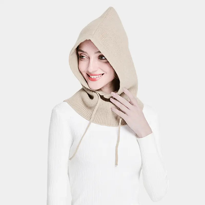 Femme souriante portant une cagoule tricot beige en maille avec capuche ajustable, idéale pour un look chaleureux et confortable.