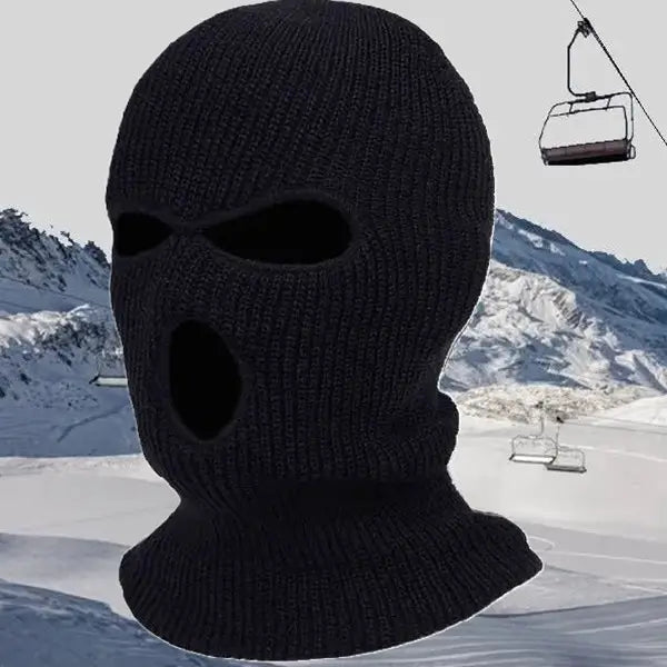 Cagoule tricotée noire avec des ouvertures pour les yeux et la bouche, portée dans un paysage enneigé avec un télésiège en arrière-plan, idéale pour le froid.