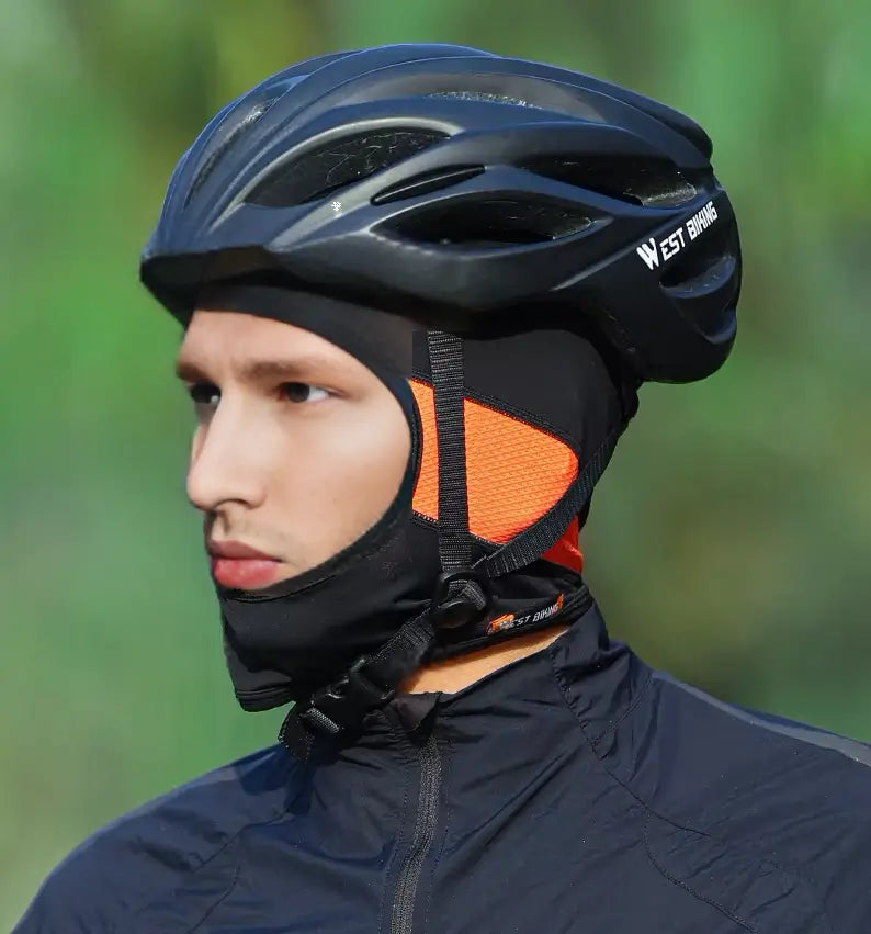 Cycliste portant une cagoule vélo en soie noire et orange sous un casque, idéale pour le confort et la protection.