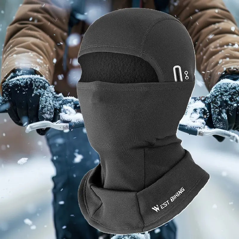 Cagoule vélo grand froid noire en tissu thermique, idéale pour le cyclisme en hiver. Design intégral couvrant le visage et le cou, avec ouverture pour les yeux, parfaite pour protéger contre le vent et la neige. Cycliste en arrière-plan pédalant dans un environnement enneigé.