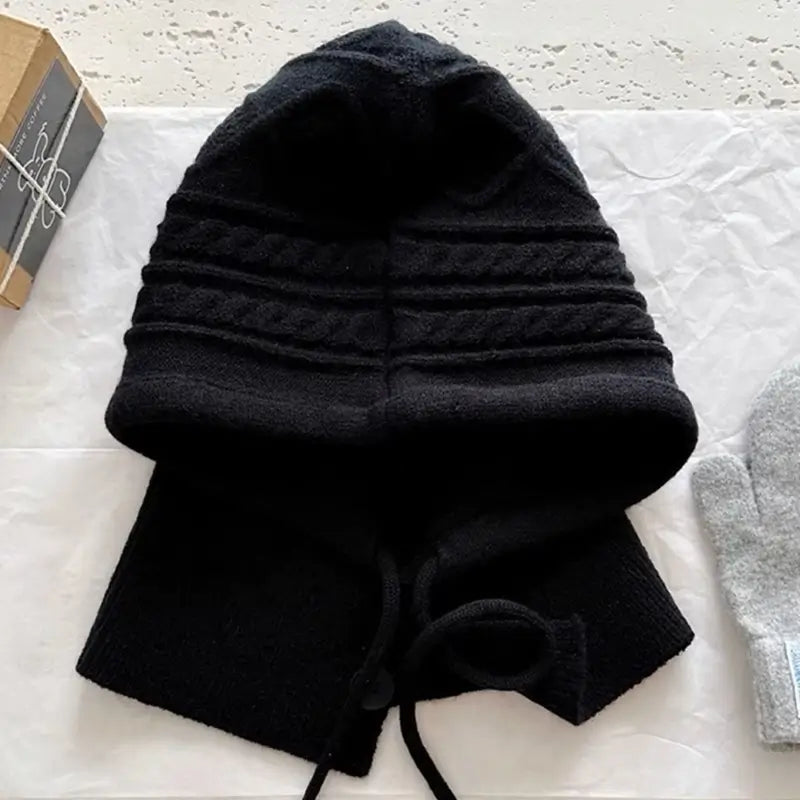 Capuche cagoule tricot noire en laine épaisse avec un design moderne et des cordons ajustables, idéale pour l'hiver.