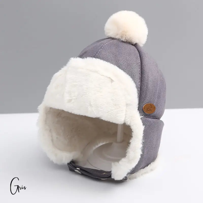 Chapka Enfant en suédine grise avec pompon blanc et intérieur en fausse fourrure douce, vue de dos sur un fond neutre. Protection hivernale idéale avec un design aviateur.