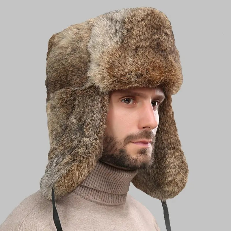 Homme portant une Chapka Russe pour Homme en fausse fourrure marron avec rabats d'oreilles abaissés, fond gris neutre, look élégant et hivernal.